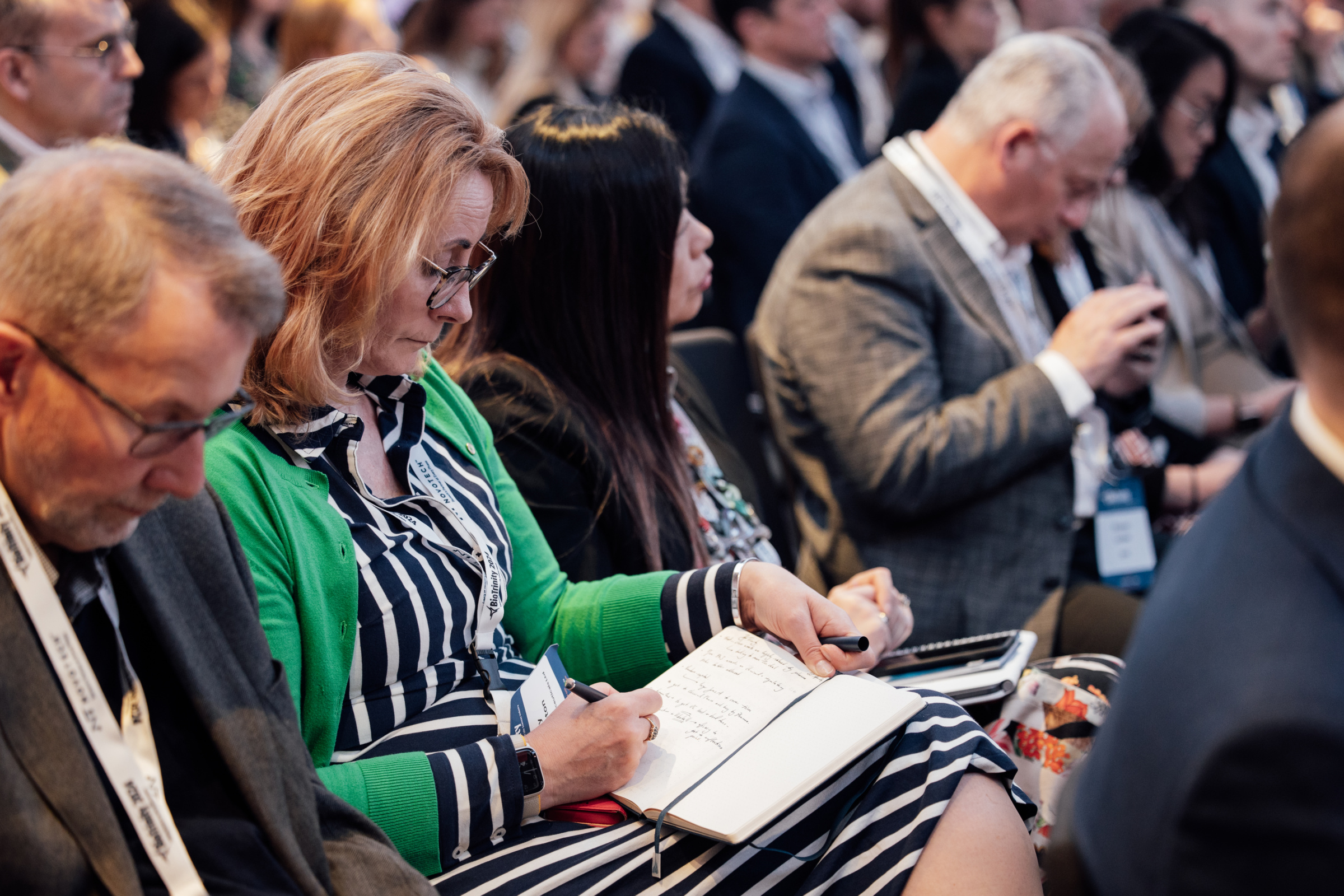 Photograph of an audience at a conference, listening and writing notes.